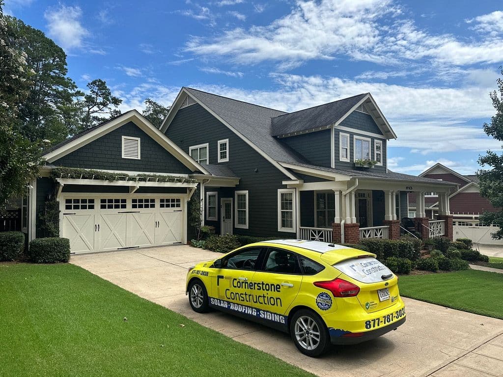 A yellow Cornerstone Construction car parked outside a dark house with white trim.