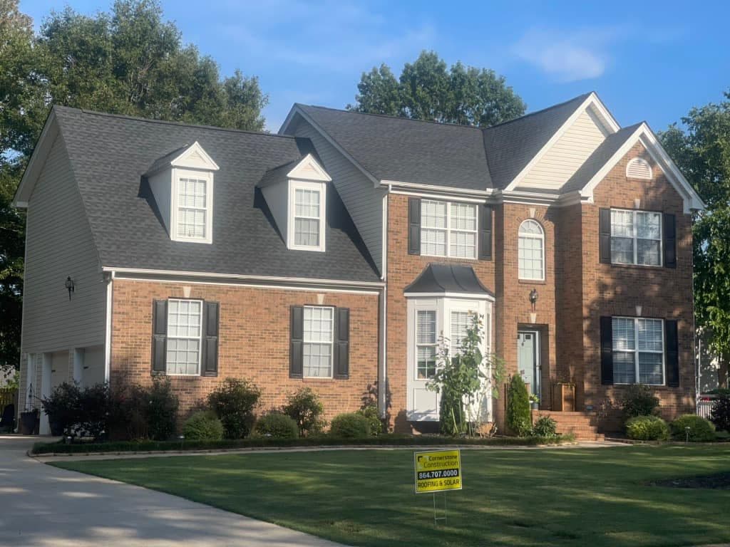 A red brick house with black shutters and new gray asphalt roofing.