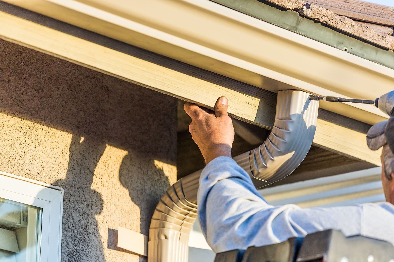 A worker installs new rain gutters and a downspout.