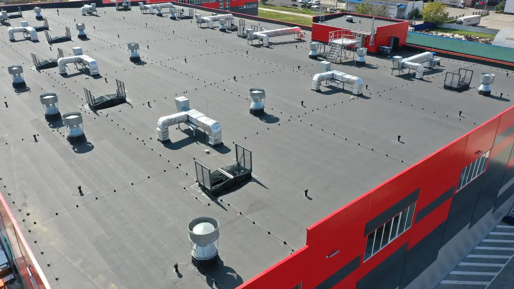 An aerial view of a red, black, and gray commercial building with newly-installed gray roofing.