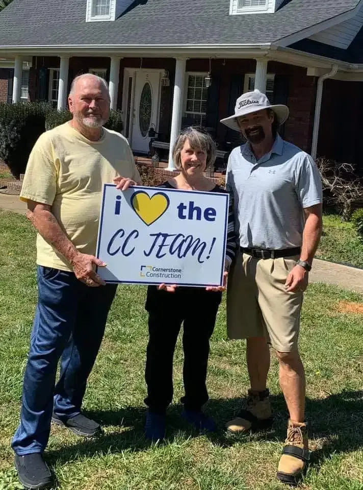 Homeowners smile holding a Cornerstone Construction sign.