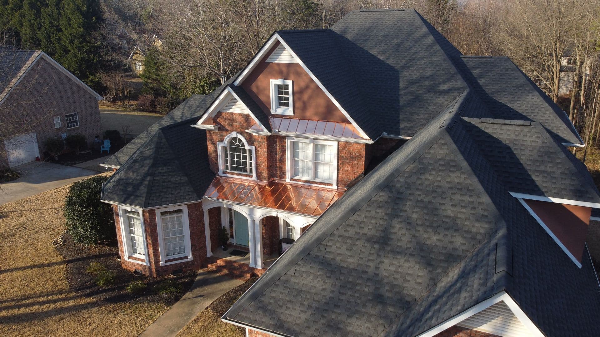 A red brick house with black asphalt shingle roofing, copper flashing, and new gutters.