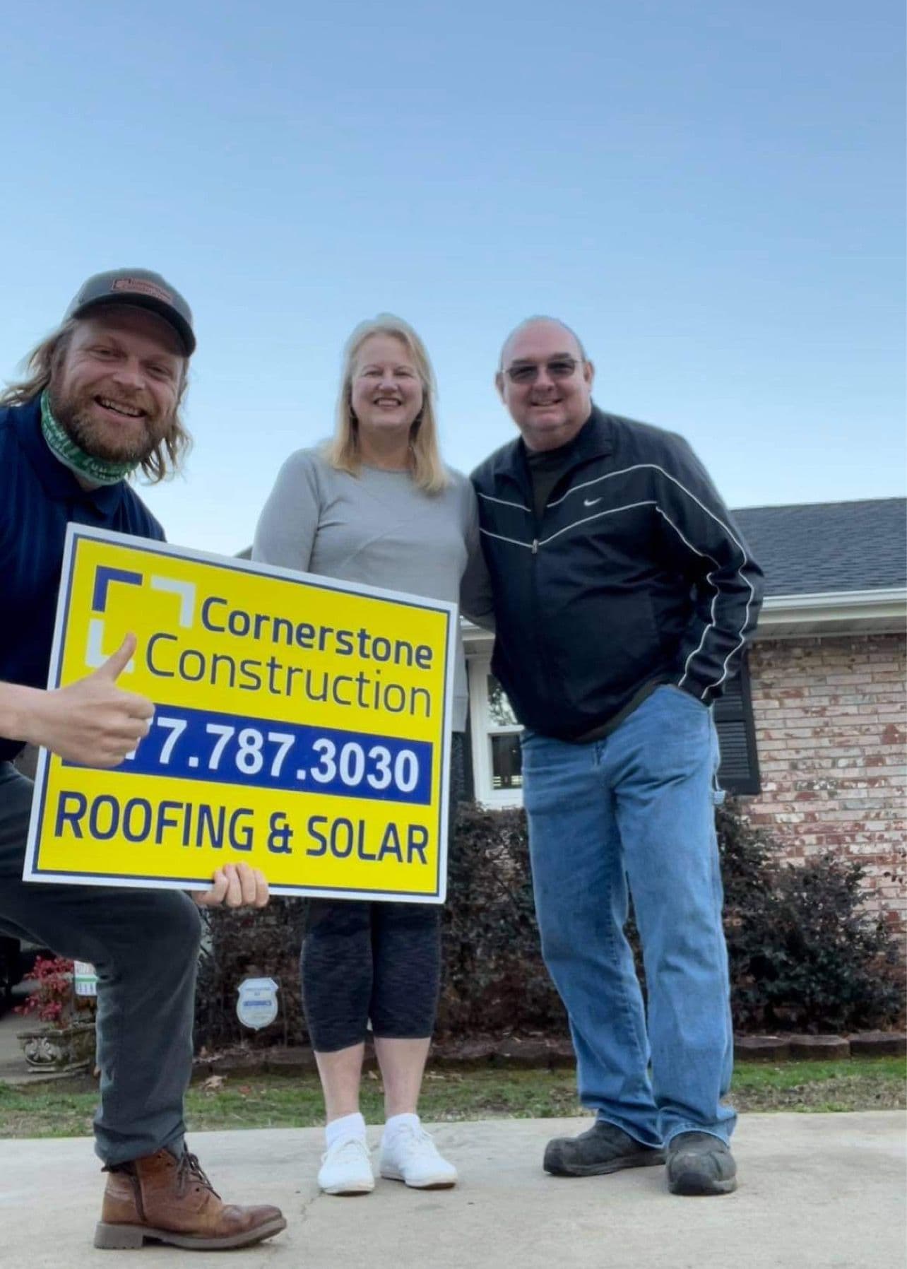 Homeowners smile holding a Cornerstone Construction sign.