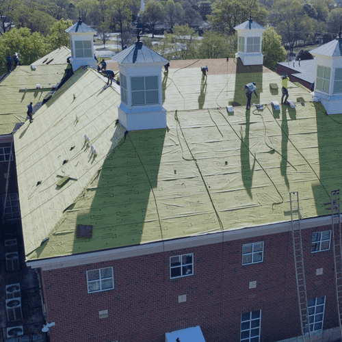 Workers install roofing on a building with four cupolas.
