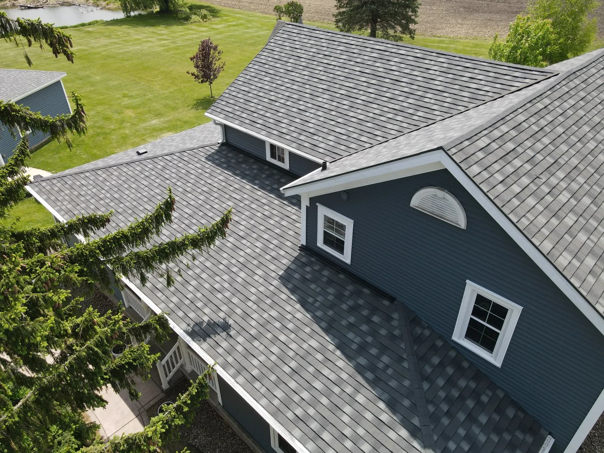An aerial view of new gray asphalt shingle roofing on a dark gray house with white trim.