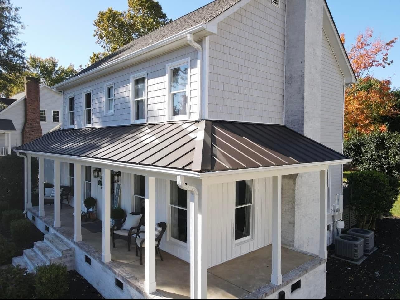 A white house with a covered porch with new dark-colored black metal roofing and white gutters.