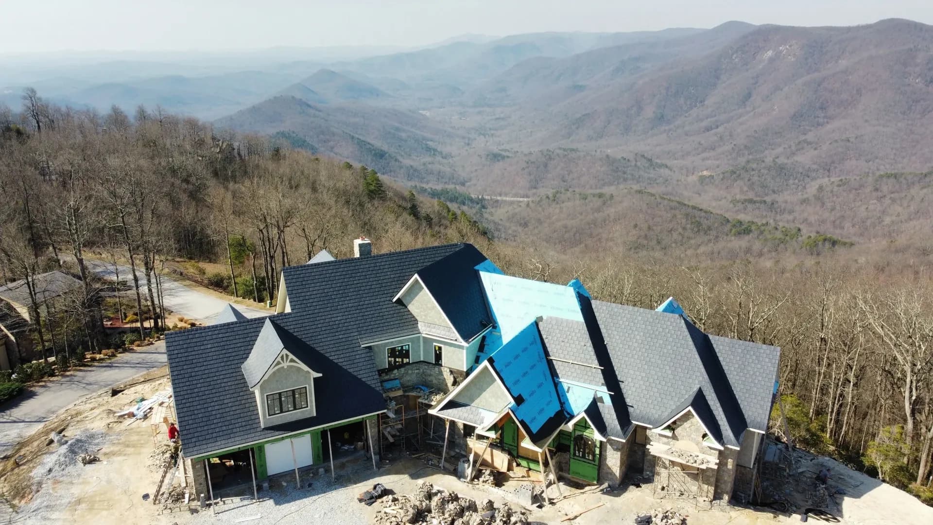 An aerial view of roofing being installed on a house. Hills are visible in the far background.