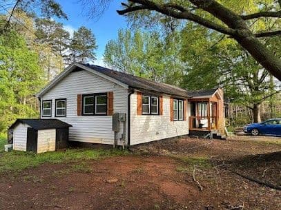 A white house with brown shutters and a damaged shingle roof.
