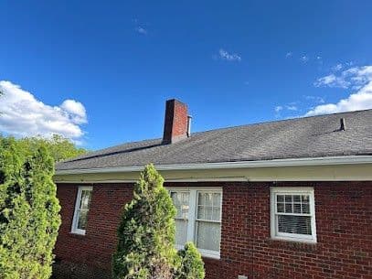A gray shingle roof with a chimney on a red brick house with white trim.