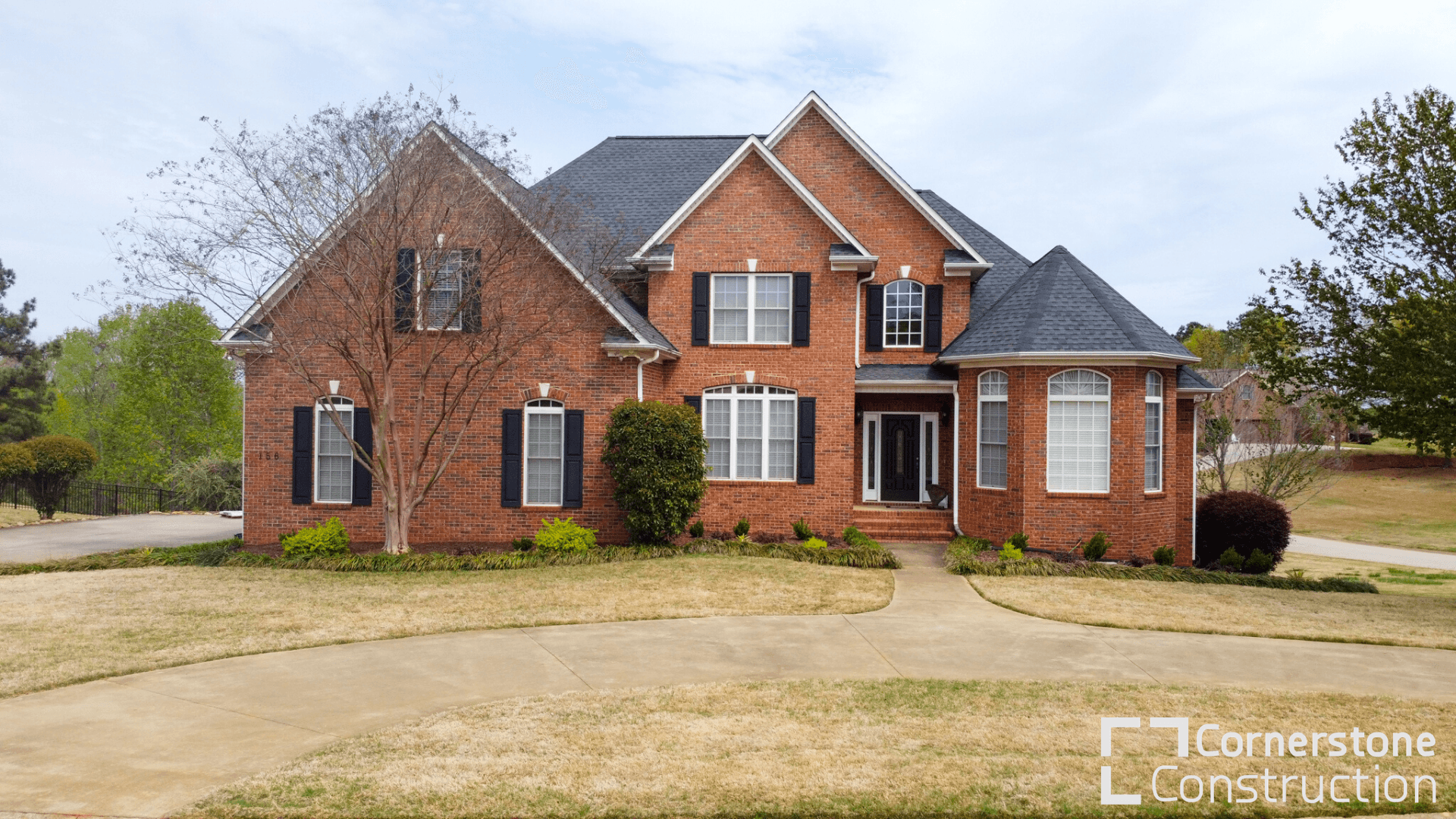 A red brick house with black shutters and new gray asphalt roofing.