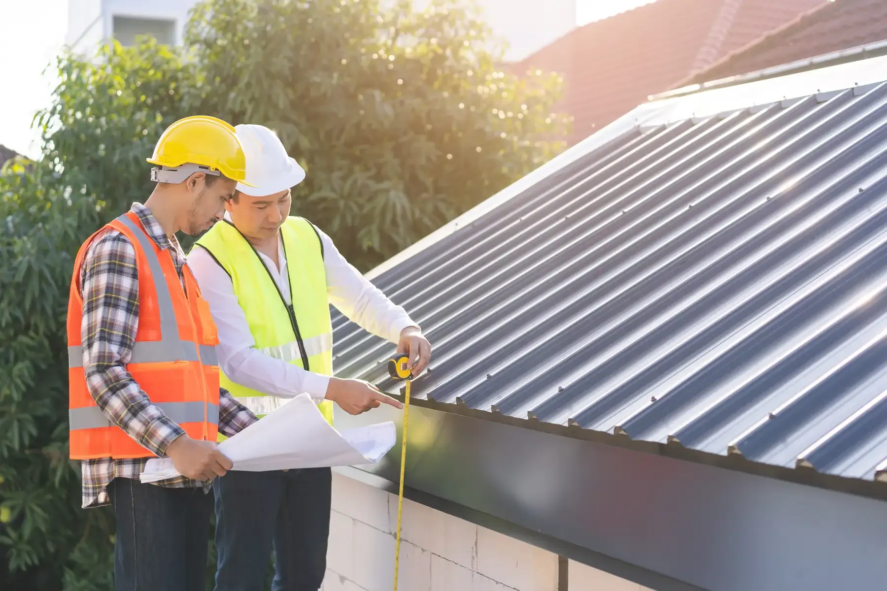 Two workers wearing hardhats take measurements on a roof.